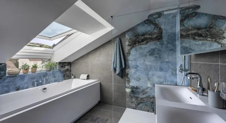 Bagno sottotetto basso con vasca, doccia con piastrelle blu marmorizzate e lucernario.
