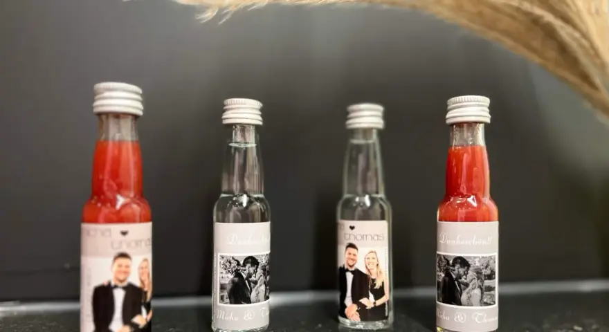 Vier kleine Flaschen mit personalisierten Etiketten, die Hochzeitsfotos und Namen zeigen. Perfekt als Schnaps zum selber machen für Gäste.