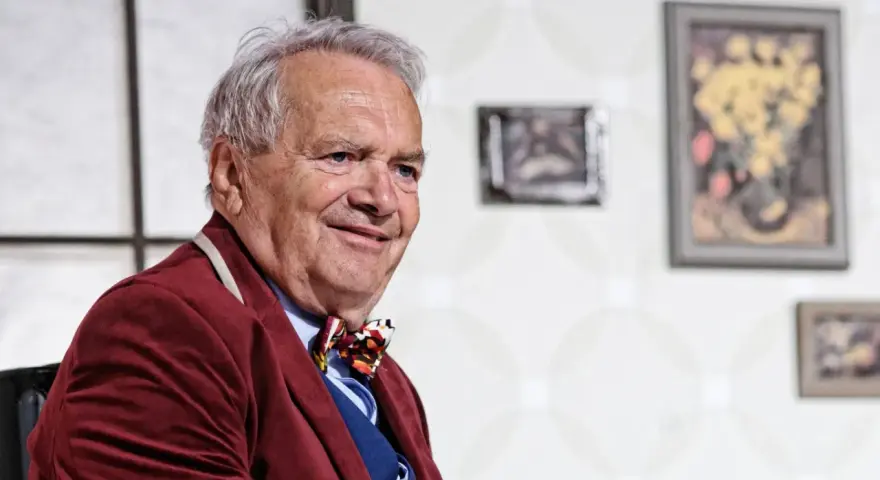 Uśmiechnięty Zdzisław Wardejn, znany z wielu filmów, w bordowym marynarkowym stroju i kolorowym krawacie.