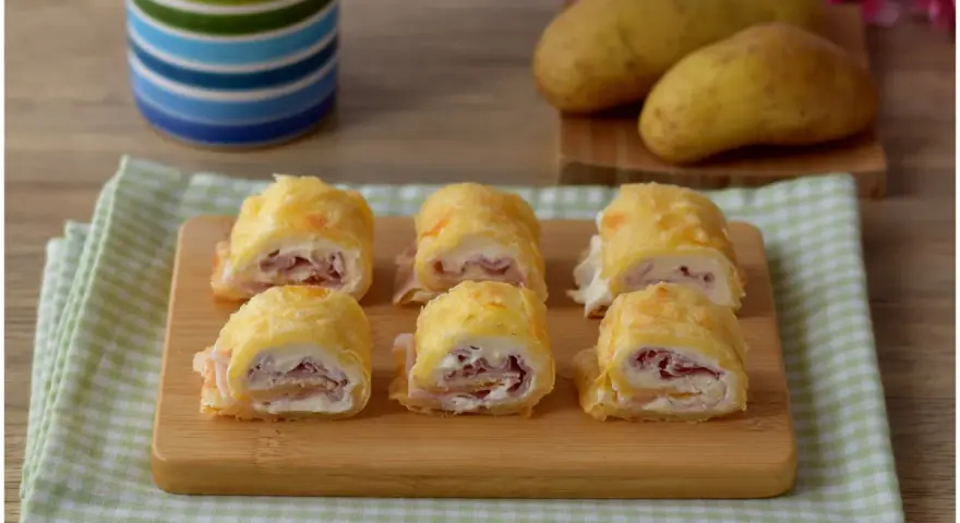 Sei rotoli di patate ripieni di prosciutto e formaggio cremoso, pronti per essere gustati.