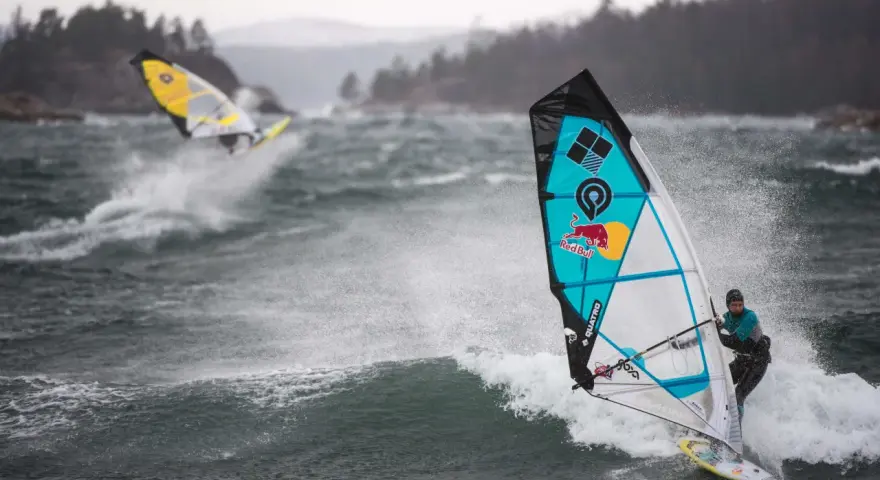 Windsurferzy na falach, jeden z nich na pierwszym planie, w akcji.