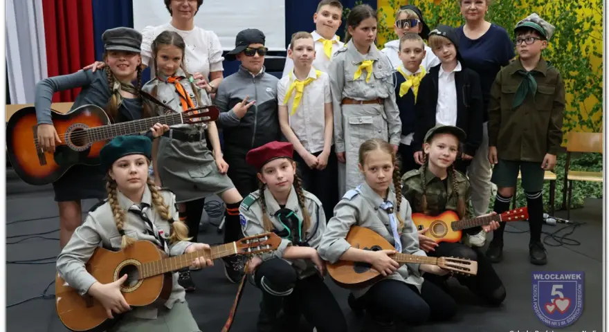 Dzieci w strojach harcerskich grają na gitarach i mandolinie. To może być zapowiedź piosenki o harnasiu.