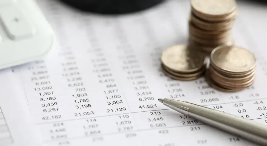 Monedas apiladas sobre un informe financiero, con una calculadora y un bolígrafo. El informe muestra números, quizás el modelo 420.