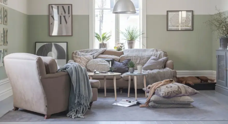 Vardagsrum i svensk stil med bekväm soffa, fåtölj och en sovande hund. Vårljus strömmar in genom fönstret och skapar en mysig atmosfär.