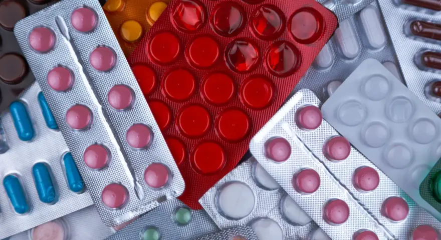 Zbliżenie na opakowania leków w blistrach: różowe, czerwone, niebieskie i białe tabletki.