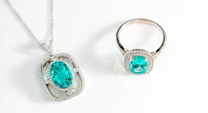 Conjunto de collar y anillo con una deslumbrante piedra de geminis turquesa rodeada de diamantes, sobre fondo blanco.