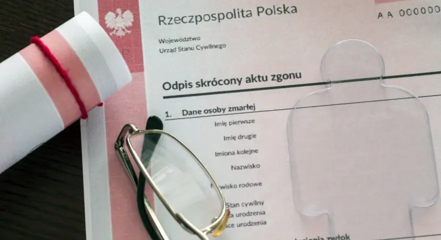 Zrolnowany dokument z orłem, okulary i formularz "Odpis skrócony aktu zgonu".