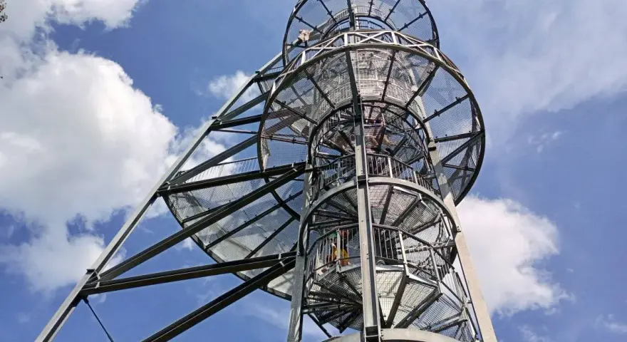 Metalowa wieża widokowa na Młynicy z krętymi schodami pnącymi się ku niebu. Widać ludzi wspinających się na szczyt.