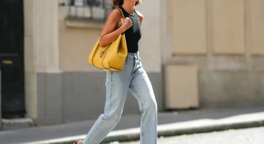 Mujer con vaqueros anchos de tiro alto, un top negro y un bolso amarillo vibrante. Un ejemplo de los diversos tipos de vaqueros mujer.