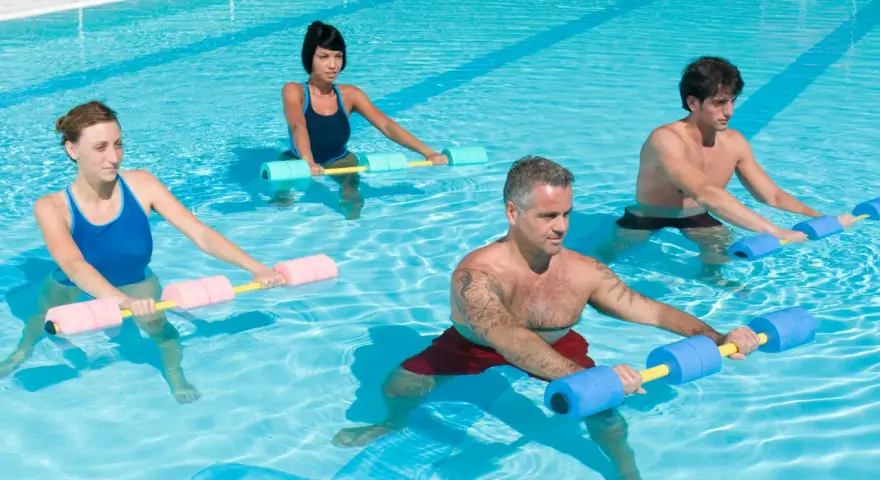 Quatre personnes font un exercice piscine avec des haltères flottants. L'eau bleue reflète la lumière du soleil.