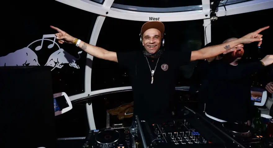 Un dj rap souriant, casqué, bras écartés, anime la soirée dans une cabine panoramique.