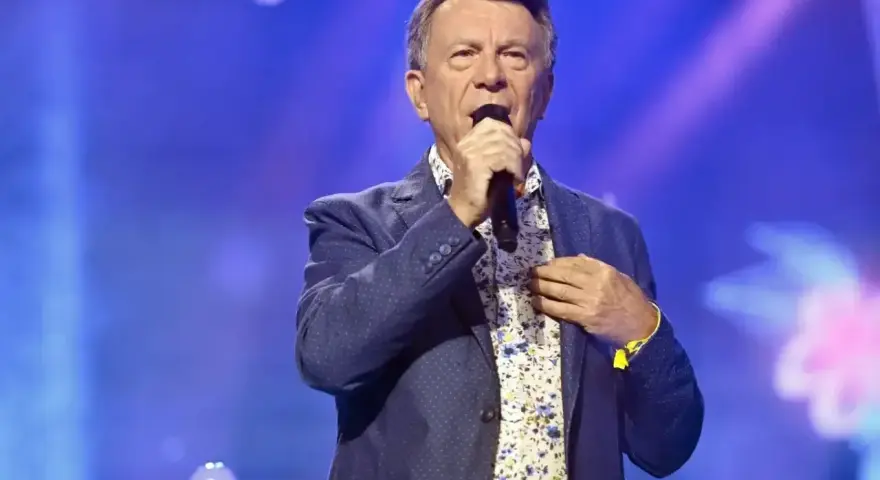Wojciech Gąsowski w niebieskiej marynarce w kropki i kwiecistej koszuli śpiewa na scenie.