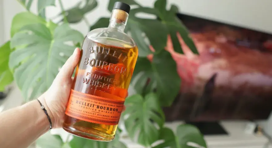 Dłoń trzyma butelkę Bulleit Bourbon. To Kentucky Straight Bourbon Whiskey, idealny do drinków.