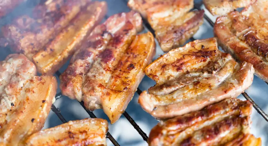 Kawałki soczystego boczku surowego pieką się na grillu, otoczone dymem.
