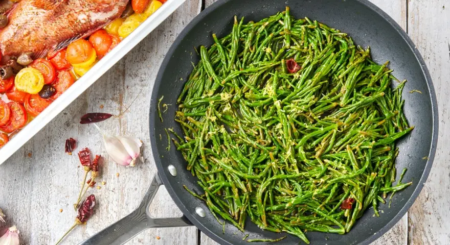 Asparagi di mare saltati in padella con aglio e peperoncino, accanto a un pesce al forno con pomodorini.