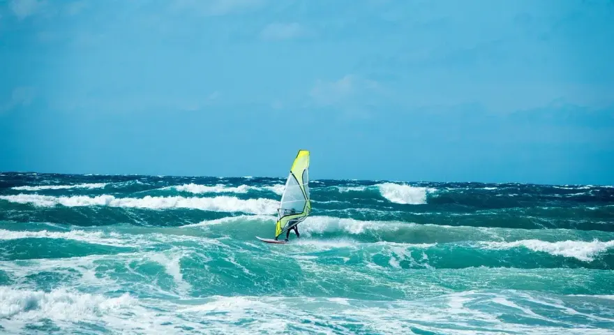 Windsurfer na wzburzonym, turkusowym morzu pod błękitnym niebem.