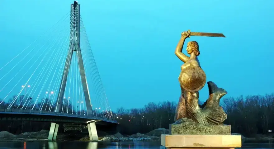 Warszawska Syrenka, bohaterka legendy, stoi dumnie z mieczem i tarczą. W tle widać nowoczesny most.