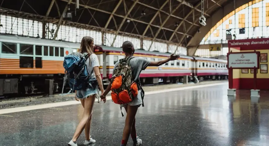 Dwie podróżniczki z plecakami idą wzdłuż peronu, gdzie stoi długi pociąg. Może to być ich pierwszy pociąg Eurostar.