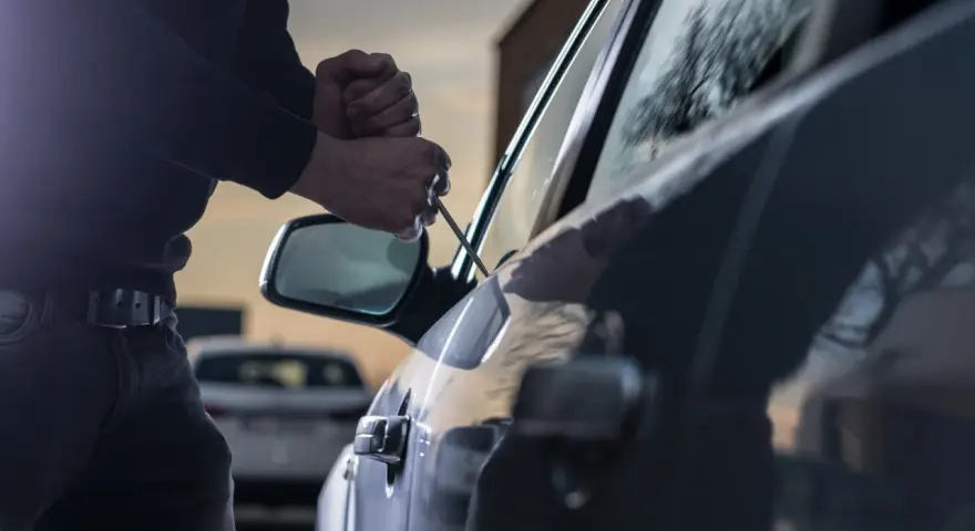 Tentativo di furto d'auto: un uomo usa un cacciavite per forzare la portiera, un'azione che rientra nella verifica veicoli rubati.