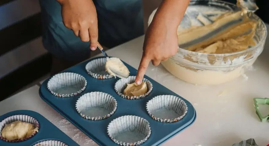 Dziecko nakłada ciasto na muffinki łyżką do formy.