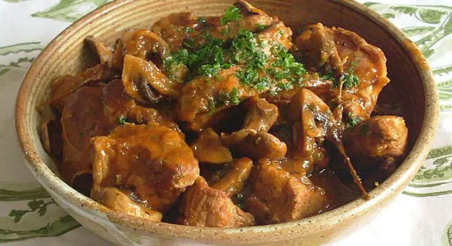 Un délicieux sauté de veau aux champignons, garni de persil frais, servi dans un bol en terre cuite.