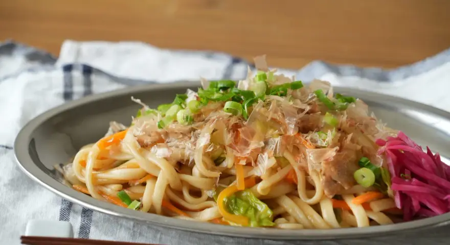 Makaron udon z warzywami, posypany szczypiorkiem i płatkami bonito, na talerzu.