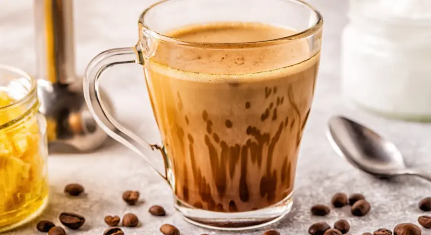 Kawa bullet coffee w szklance, obok ziarna kawy, słoiczek z miodem i łyżeczka.