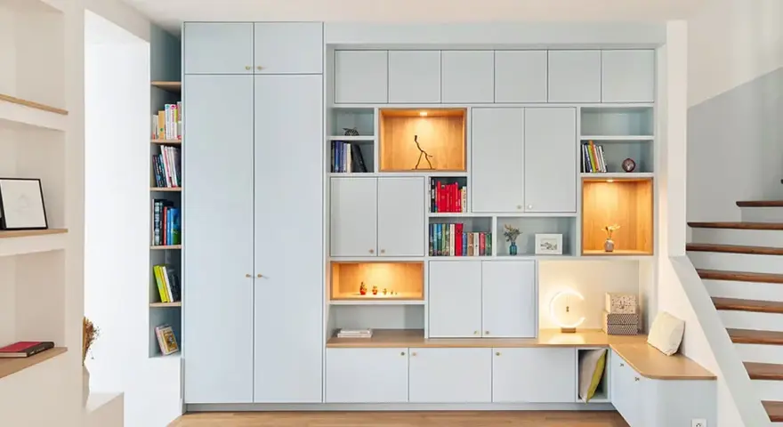 Aménagement d'un **pièce à vivre** moderne avec bibliothèques modulables, rangements intégrés et un banc cosy près de l'escalier.