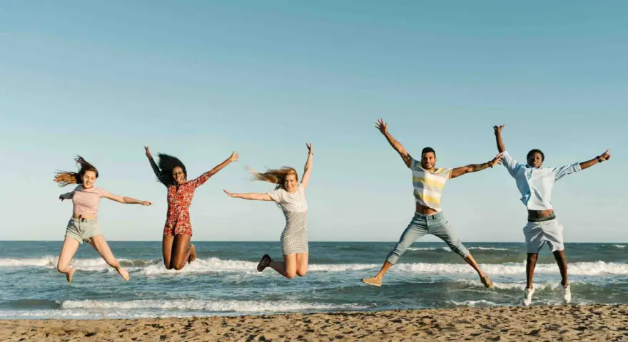 Fünf junge Leute springen ausgelassen am Strand. Sie freuen sich über ihr Sprachreise Stipendium und die Freiheit.