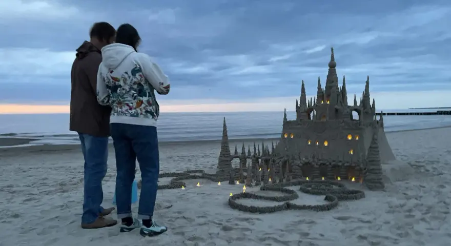 Para podziwia imponujące zamki z piasku na plaży, w okolicach Kołobrzegu. Wieczorne światła dodają magii.