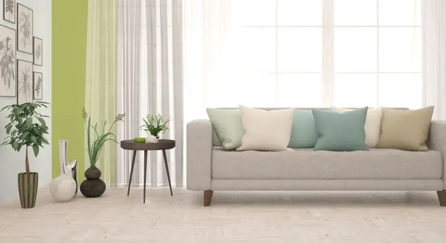 Jasny salon z kanapą i poduszkami w pastelowych kolorach. Ściany w odcieniu oliwkowym tworzą przytulną atmosferę.