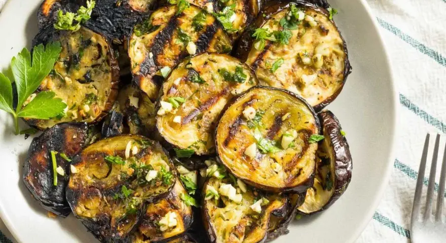 Rodajas de berenjenas a la plancha, doradas y tiernas, con ajo picado y perejil fresco. Un plato sencillo y delicioso.