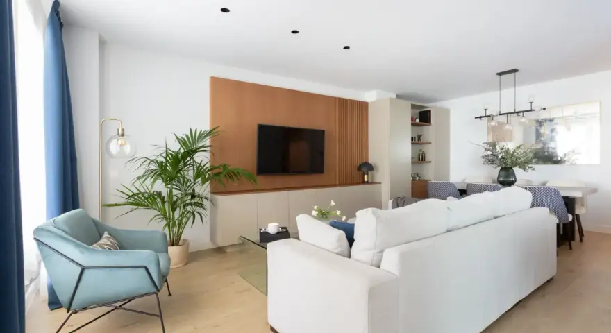 Un elegante salón moderno blanco con sofá, sillón azul, planta y mesa de comedor.