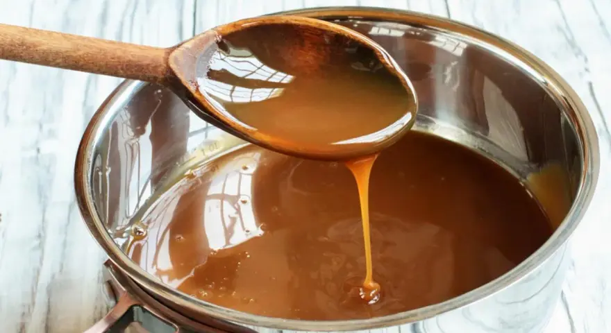 Caramelo líquido cayendo de una cuchara de madera a una olla, perfecto para tu flan al estilo Eva Arguiñano.
