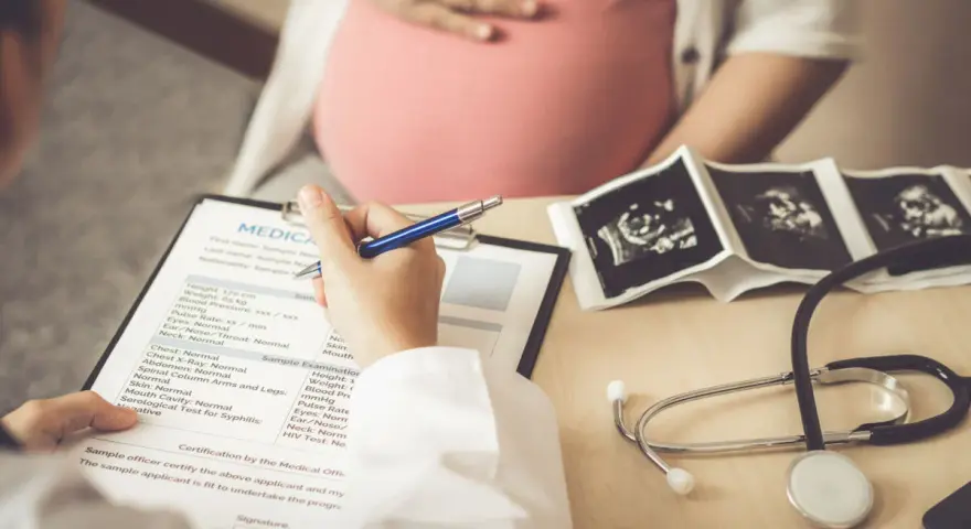 Medico compila cartella clinica con ecografie e stetoscopio. L'autismo si può diagnosticare in gravidanza, con controlli precoci.