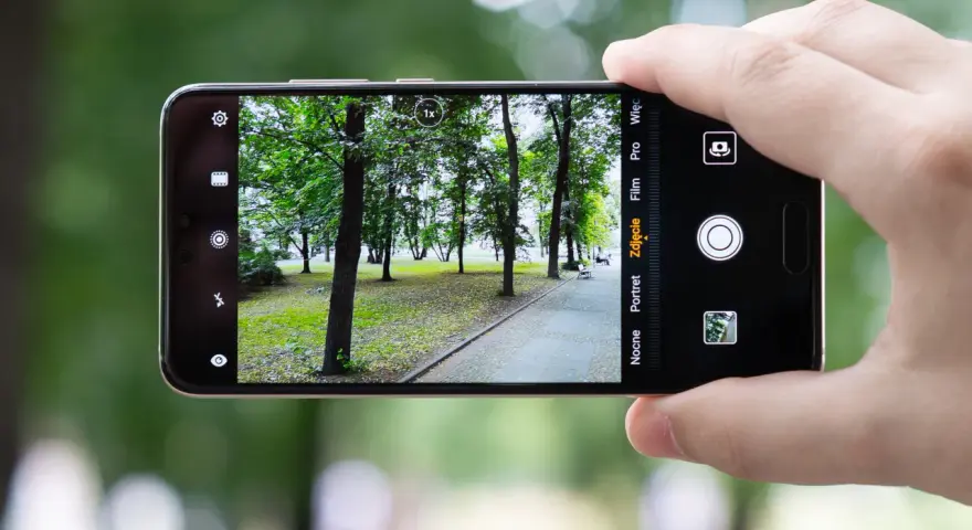 Dłoń trzyma smartfon Huawei P20, aparat kadruje parkowy krajobraz z alejką i drzewami.