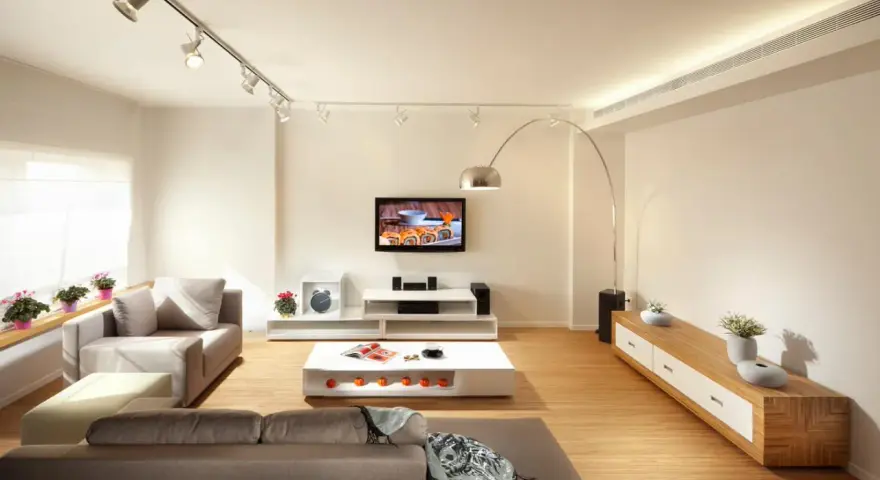 Iluminar un salón moderno con luces de riel y lámpara de arco. Sofás grises, mesa de centro blanca y mueble de TV.