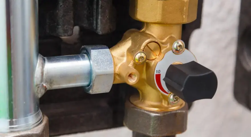 Dettaglio di una valvola pressione acqua caldaia in ottone con manopola nera e indicatore numerico.