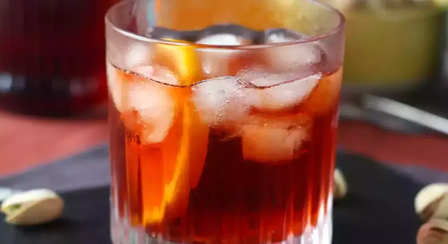 Szklanka z czerwonym drinkiem, lodem i plasterkiem pomarańczy.
