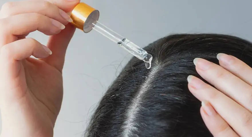 Eine Hand trägt mit Pipette ein Serum auf die Kopfhaut auf, um trockene Schuppen loswerden.