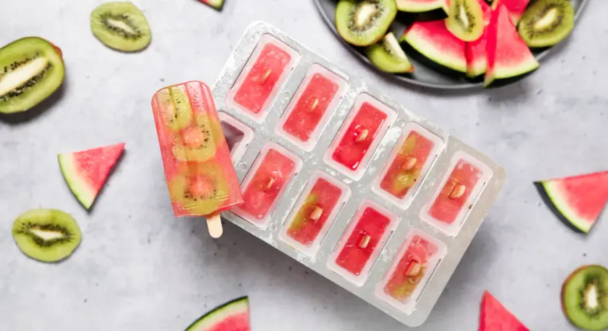 Erfrischendes Melonen-Kiwi-Eis in einer Form, daneben frische Früchte. Perfekt für heiße Tage!