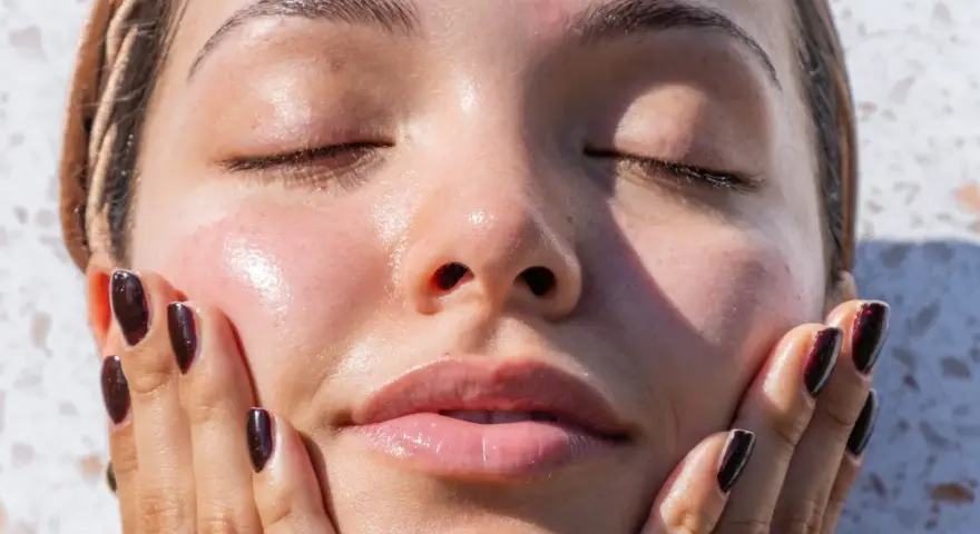 A woman's face, with eyes closed and skin glowing, touches her cheek. It makes you wonder, can your skin type change with the seasons?