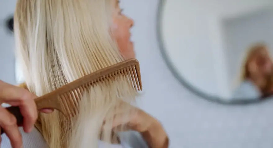 Kobieta czesze blond włosy, szukając rozwiązań co na wypadanie włosów po ciąży.