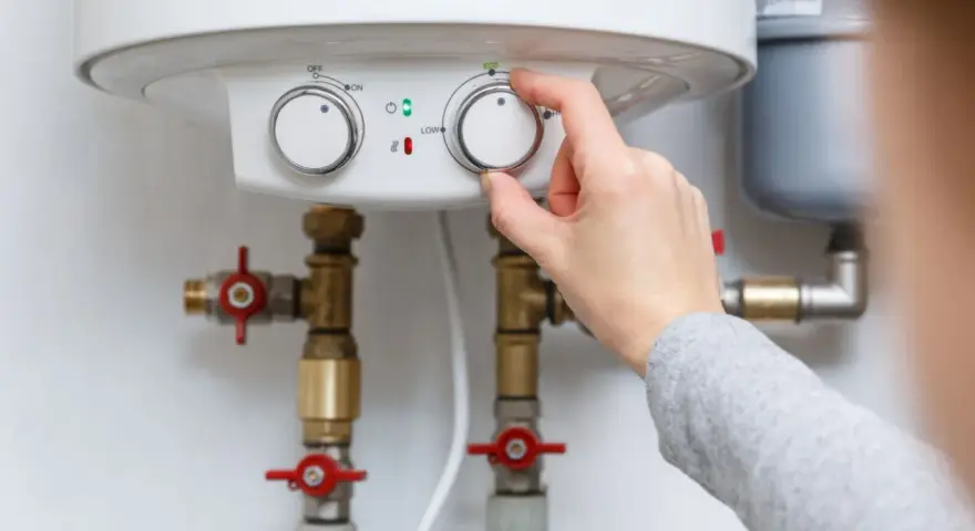 Adjusting the temperature dial on a water heater, showing its plumbing connections.