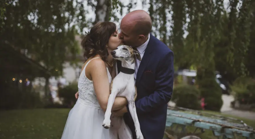 Un couple s'embrasse tendrement, tenant leur chien, dans cette photo de mariage.