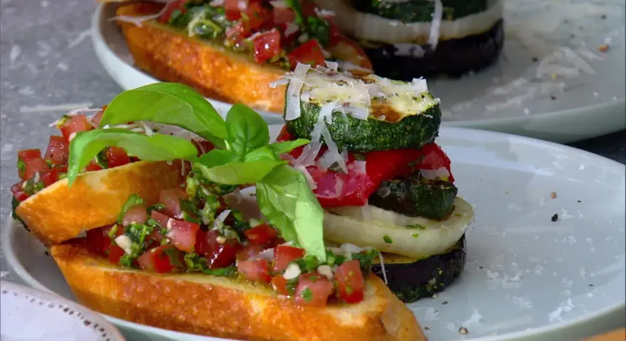 Vegane Grillrezepte: Bruschetta mit Tomaten und gegrilltem Gemüse-Turm, garniert mit Basilikum und Parmesan.