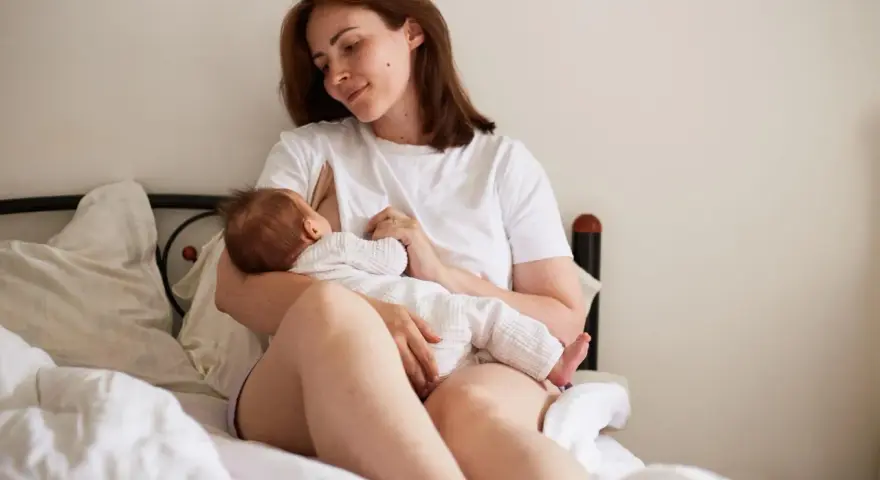 Matka karmi piersią dziecko na łóżku. To piękny obrazek z okresu 12-miesięczny okres ochronny po urlopie macierzyńskim.