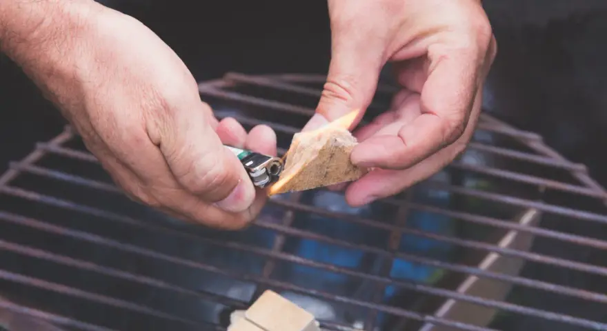 Hände zünden Grillanzünder an, um den Grill anzufeuern.