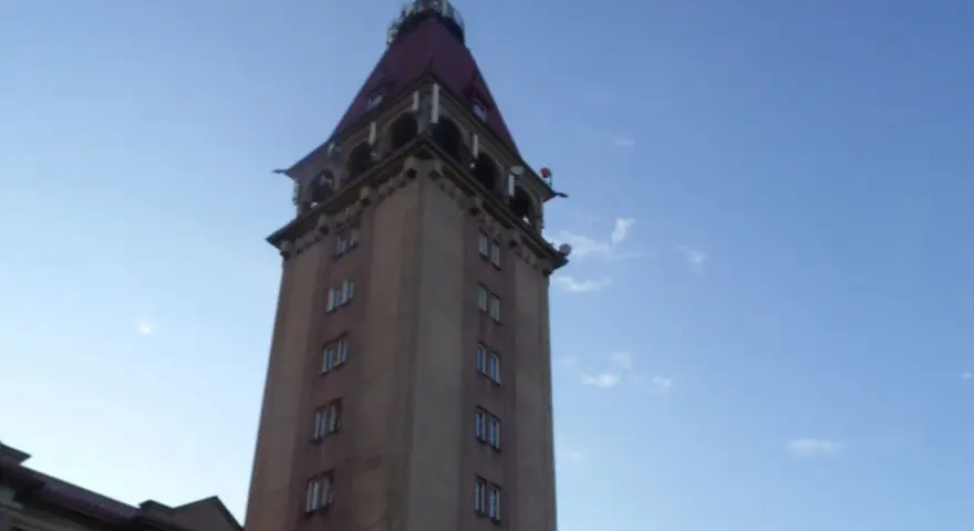 Wysoka wieża z czerwonym dachem, przypominająca dom rybaka, na tle błękitnego nieba.
