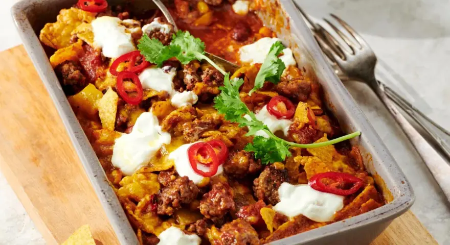 Herzhafter Shepherd's Pie mit Hackfleisch, Tortilla-Chips, Chili-Ringen und Klecksen saurer Sahne, garniert mit Koriander.